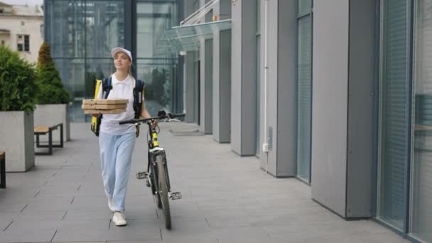 漂亮的女人骑自行车跑来跑去的商务中心 走到定制和持有比萨在她的手中 速递邮差及速递服务概念 — 图库视频影像
