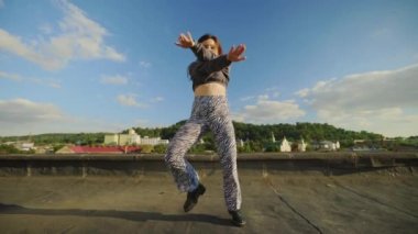 Havalı, yetenekli hip-hop kızı çatıda dans ediyor kameraya bakıyor ve dışarıda inanılmaz jestler ve hareketler yapıyor. Kadın sanatçı performansı. Sokak dansı