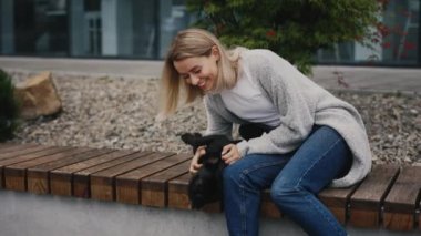 Kafkas sahibi New Modern Park 'ta Bench' te oturuyor ve Fransız Bulldog 'uyla oynuyor. Park Bench 'te otururken evcil hayvanını okşayan bir kadın. Halk ve Köpekler Dostluk Konsepti