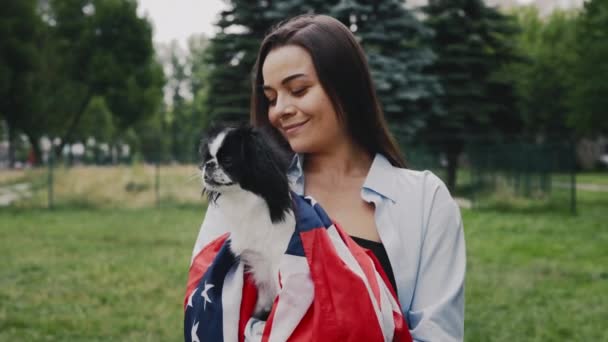 快乐的白人女人牵着她的日本金狗 裹在美国国旗里 站在公园外面 人与狗的爱国主义概念 — 图库视频影像