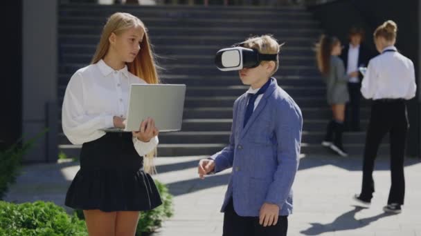 两名在外面工作的小职员使用虚拟现实耳机 男孩戴着Vr眼镜 女孩在笔记本电脑上工作 使用Vr未来技术的儿童 — 图库视频影像