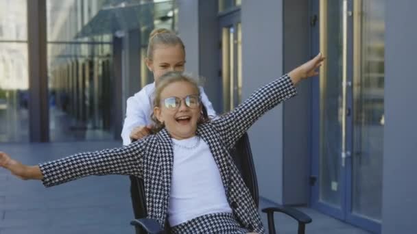Dwie Podekscytowane Mała Bizneswoman Bawiąc Jazda Krzesłach Biurowych Poza Budynkiem — Wideo stockowe