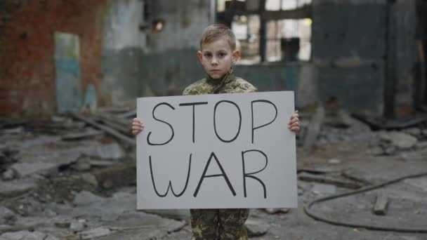 軍の制服抗議戦争を身に着けている少年の肖像 碑文停止戦争とバナーを保持 男性キッズアクティビティカメラを見ています 戦争に反対する子供 パトリオット — ストック動画
