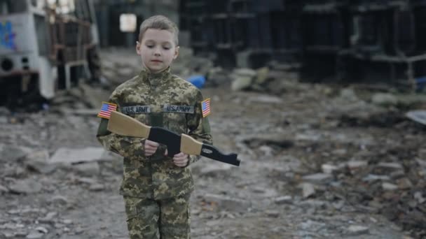 小美国士兵拿着玩具枪在废墟的背景下行走被毁的工厂 任务中的战士 美国爱国者 现代战争和战斗概念 — 图库视频影像