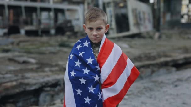 在废墟背景下站在美国国旗下的小爱国美国士兵的画像 男孩爱国者看着相机 独立日 — 图库视频影像