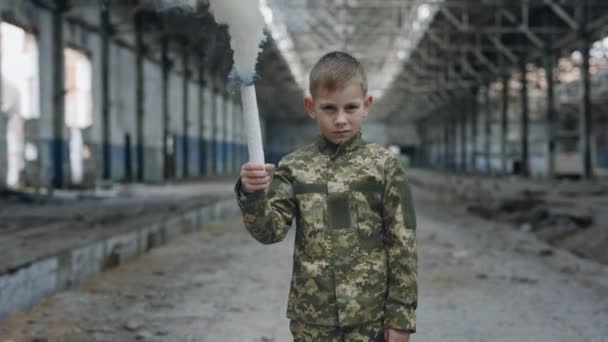 破壊された惑星を歩く手の中に白い煙爆弾を持っている軍の制服を着た少年兵士 肖像画 危険警告 子供は助けを求めています 戦争だ — ストック動画