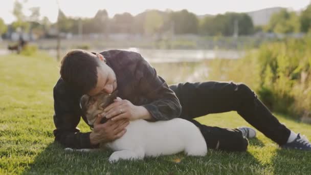 公園に横たわる白人スタイリッシュな男 ストローキング 彼のブルックリンブルドッグへの愛を示す 公園の芝生の上に寝そべっている間に犬を引っ掻いている男 人と犬の友情の概念 — ストック動画