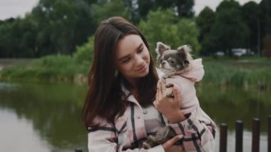 Genç ve güzel mutlu kadının portresi, sevimli küçük Chihuahua 'sını taşıyor. Yerel Gölü ve Park Arkaplanındaki Kameraya Bakan Şirin Kız. Halk ve Köpekler Dostluk Konsepti