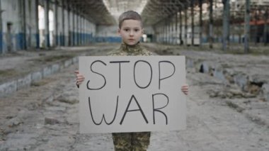 Askeri üniformalı küçük çocuğun portresi savaşı protesto ediyor, yazıtla savaşı durduruyor. Kameraya bakan Erkek Çocuk Aktivisti. Savaşa Karşı Çocuk. Vatansever