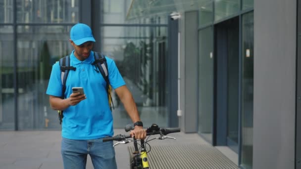 Улыбающийся Афроамериканец Синей Униформе Ходит Бизнес Центру Велосипедом Принимает Заказы — стоковое видео