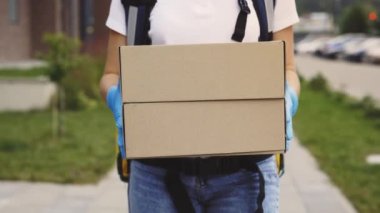 Kadın Kurye, Müşteri İçin Eldivenlerinde Koruyucu Eldiven Kutusu Taşıyor, Dışarı Çıkıyor, Müşteri Buluyor. Yiyecek, Mal Teslimatı. Salgın sırasında kız kurye. Kapat.