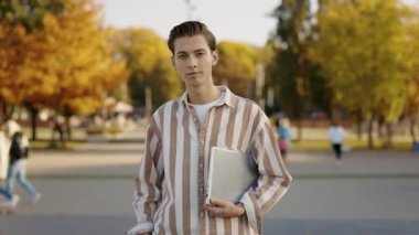Beyaz adamın portresi caddede dikilip kameraya bakıyor ve dizüstü bilgisayarı tutuyor. Parkta çalıştıktan sonra Vasual giysiler giyen yakışıklı bir genç.