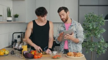 LGBT Çifti Mutfak ve Aşçılık 'taki Yeni Apartmanlarında Birlikte Ayakta Duruyorlar, Bir Partner Tablet' ten Farklı Tarifler Gösteriyor. Teknoloji, İnsanlar ve LGBT Kavramı