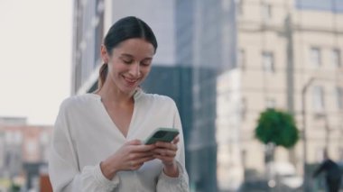 Çekici Gülümseyen İş Kadını Bir Şehir Bölgesi 'nde Dururken Cep Telefonu Uygulaması Kullanıyor. Akıllı Telefon Ekranı 'na bakıyor ve Mutlu Hissediyor. 