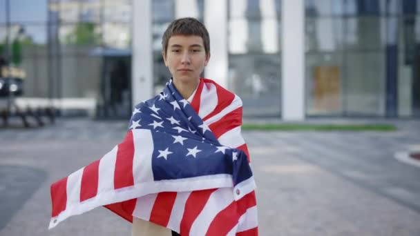 严肃的白人妇女自豪地代表着她的祖国 并把美国国旗背在她的背上 时尚的美国女商人在慢动作的户外佩带美国国旗是爱国主义的标志 — 图库视频影像