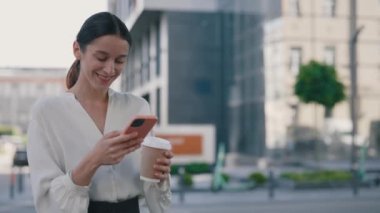 Kahve molasında ofis binasının yanında dururken Smartphone kullanan mutlu iş kadını. Akıllı Telefon Tutma İçeceğine Bakan Kadın. Teknoloji, Halkla İletişim Konsepti