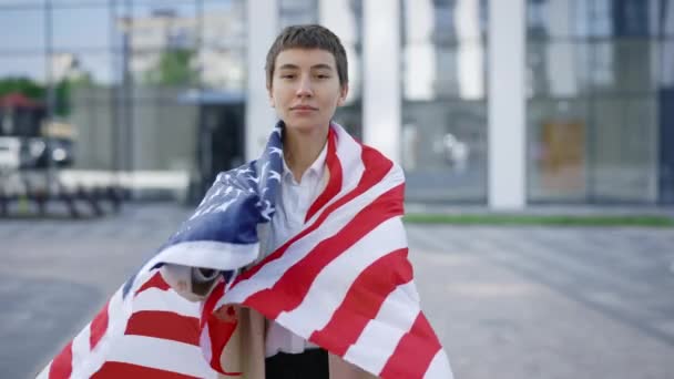 迷人的白人妇女自豪地代表着她的祖国 并把美国国旗放在她的背上 时尚的美国女商人在慢动作的户外佩带美国国旗是爱国主义的标志 — 图库视频影像