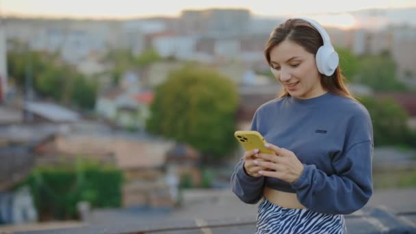 Junge Kaukasierin Mit Kopfhörern Und Smartphone Auf Dem Dach Frau — Stockvideo