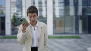 Çekici beyaz kadın patron resmi takım elbise giyip cep telefonundan sesli mesaj kaydediyor. İş merkezinin yakınındaki Mutlu Kadın Yapay Zeka Araması İçin Akıllı Telefondan Komut Okuyor