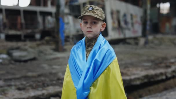 遺跡の背景にあるウクライナ国旗に包まれた小さなウクライナ愛国兵士 男性兵士の肖像カメラを見ている ウクライナでの戦争 戦士よ シンボル — ストック動画