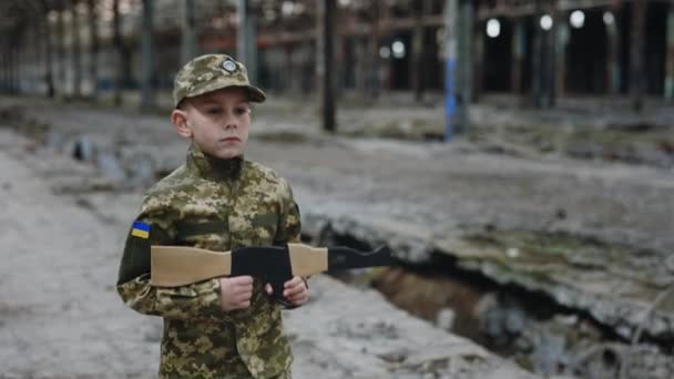 Ένα Μικρό Αγόρι Στρατιωτική Στολή Πλησιάζει Ένα Κατεστραμμένο Εργοστάσιο Κρατώντας — Αρχείο Βίντεο