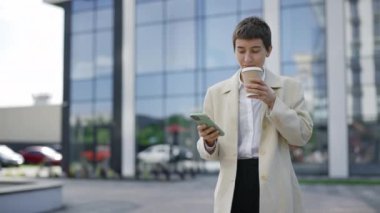 Resmi Kahverengi Takım Elbisesiyle Yürüyen Mutlu İş Kadını Portresi Cihazını Kullanmak ve İş Sohbetlerine Cevap Vermek. Kadın Patron İş Yeri 'ne yakın. Smartphone' daki Uygulamalarla Mesajlaşıyor ve Kaydırıyor. Kahve İçiyor
