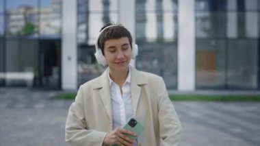 Neşeli Çekici Kız Takım Elbiseli Açık havada Dans Etmek Modern Şehir 'de Akıllı Telefon Müzik Uygulaması Kullanmak. Gülümseyen İş Kadını Şehir Caddesinde Dinleniyor. Halk ve Müzik Konsepti