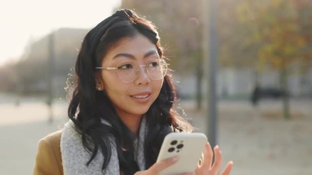 Χαρούμενη Ασιάτισσα Μαθήτρια Που Περπατάει Έξω Κρατώντας Κινητό Της Και — Αρχείο Βίντεο