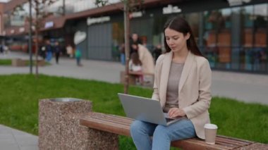 Gündelik Akıllı Giyimli Dizüstü Bilgisayarlı Kafkas İşadamı Arka planda İş Merkezi ile Bench 'te otururken çalışıyor. Genç İş Kadını Uzakta Çalışıyor