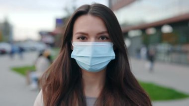Koruyucu tıbbi maske takan ve sokakta dikilen güzel siyah saçlı genç bir kadının portresi. Güvenli ve Mutlu Kadın Sosyal Mesafe Uygulaması, Karantina