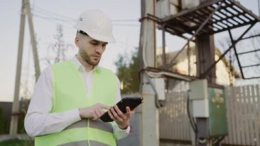 Dışarıda Koruma Giysileri Mühendisi Tablet Güç Hattına Not alıyor ve Sistemin Çalışmalarını Analiz Ediyor. Mimar, Mimar çalışıyor. Bakım ve Servis
