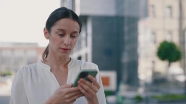 Gülümseyen İş kadını Modern Ofis Binası 'nın yanında duran akıllı telefonu kullanıyor. Akıllı Telefon Ekranı 'na Bakan ve Mutlu Hisseden Kadın. 