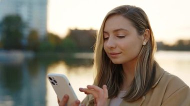 Şehir Gölü 'nün yakınındaki caddede Smartphone' unu kullanan genç kadının yakın görüntüsü. Kafkasyalı Çekici Kadın Arkadaşlarıyla Mesajlaşıyor, Sosyal Medya Kaydırılıyor