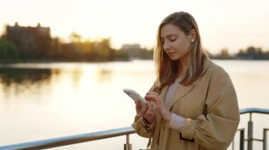 Şehir Gölü 'nün yakınındaki caddede Smartphone' unu kullanan genç kadının yan görüntüsü. Kafkasyalı Çekici Kadın Arkadaşlarıyla Mesajlaşıyor, Sosyal Medya Kaydırılıyor