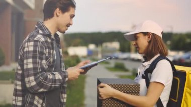 Özel Üniformalı Çekici Kadın Kurye, Sarı Sırt Çantasını Yakışıklı Adam 'a Karton Hediye Kutusu Taşıyor. Bayan İşçi Teslimatı, Karton Paketler Teslimatı. Teslimat için Erkek Müşteri İşaretleri