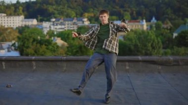 Yetenekli beyaz erkek dansçının çatıdaki dinamik hip-hop performansı. Dans tarafından büyülenen esmer adam etkileyici hareketler ve jestler sergiliyor. Etkileyici vücut kavramları