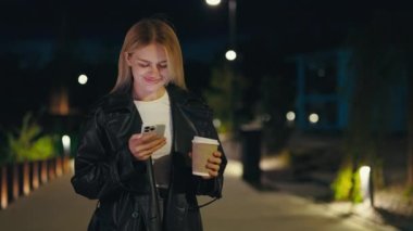 Güzel Joy Lady 'nin cep telefonunda mesajlaşması, Yalnız Gece Yürüyüşü' nde arkadaşlarına mesaj göndermesi, akşamın tadını çıkarması. Dışarıda kahve tutan kadın. Gadgets ve Teknoloji Konsepti