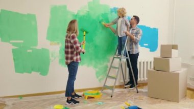 Aile duvarlarını yeşille boyuyor, çocukla birlikte elden geçiriyorlar. Karı koca oğullarıyla tadilat yapıyor ve eğleniyorlar. İç tasarım, yeni daire. Çocuk ailesine yardım ediyor.