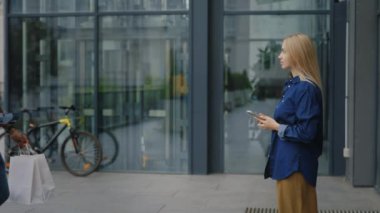 Üniformalı bir erkek kurye iş merkezindeki beyaz bir kadın müşteriye paket teslim ediyor. Müşteri paketin parasını çevrimiçi olarak NFC terminali üzerinden öder.