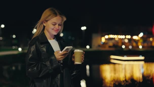 Jovencita Sonriente Parada Afuera Usando Smartphone Sosteniendo Café Para Llevar — Vídeos de Stock