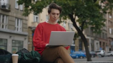 Laptop 'u dışarıda oturan ve bilgisayarda yazan adam. Dışarıdaki Beyaz Adam Uzaktan Çalışıyor. Tasasız Adam Dinleniyor ve Dizüstü bilgisayar kullanıyor. Konsept Eğitim, Öğrenci