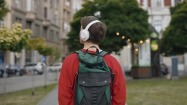 Kulaklıklı Müzik Dinleyen ve Şehirde Yürüyen Genç Adam. Yakışıklının Ses Podcast 'i ya da Kitap' ı dinlerken ve Kablosuz Aygıt Kullanırken, Açık havada yürürken görüntüsü