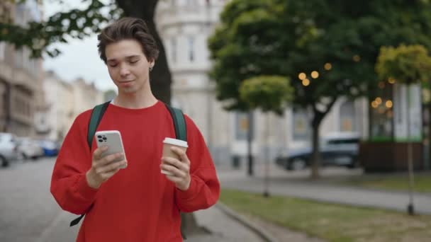 英俊的白人男子与棕色头发举行咖啡 使用电话 走在市中心的大街上 年轻学生与手机户外 慢动作人与技术概念 — 图库视频影像