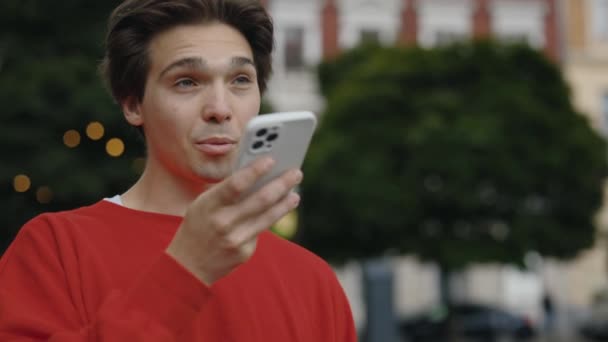 吸引人的男人在手机上制造语音信息或使用虚拟助手应用程序 年轻人在街上散步时 在扩音器上记录语音讯息 技术概念 — 图库视频影像