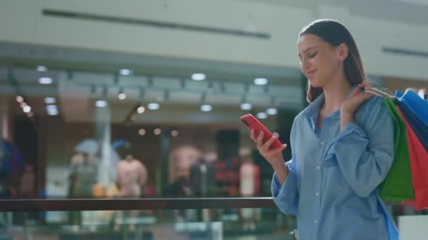 紙袋に買い物を抱えていた笑顔の客 ショッピングバッグを持っている女性は 家に帰るときに彼女の携帯電話を使用しています ショッピング後の女性 テキスト — ストック動画
