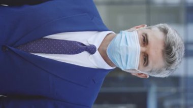 Dikey video. Tıbbi maske takan yakışıklı, beyaz bir işadamının yüzüne doğrudan kameraya bakarken. Sokaktaki bir adamın portresi. Salgın konsepti
