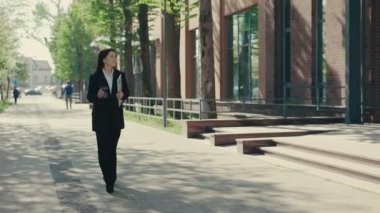 İş merkezine resmi takım elbiseli, iş için dizüstü bilgisayarını tutan ve kahve ya da çay için elinde eko bardakla giden mutlu bir iş kadını. İnsanlar ve teknoloji kavramı