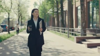 İş merkezine resmi takım elbiseli genç bir iş kadını portresi iş için dizüstü bilgisayarını tutuyor ve kahve ya da çay için elinde eko bardakla gidiyor. İnsanlar ve teknoloji kavramı