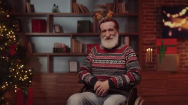 Arka planda Yeni Yıl Arifesi ile oturma odasında tekerlekli sandalyede oturan mutlu büyükbabanın portresi. Noel 'de Geyik Kapağı Giyen Yaşlı Engelli Adam. Kış Tatili ve Engelliler Konsepti