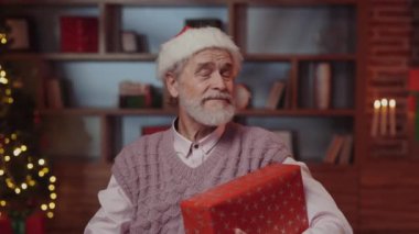 Noel Baba Başlığı Giyen Kral Yaşlı Adam 'ın portresi, Dekorasyon Odası Arkaplanda Oturması ve Yeni Yıl Hediyesi Tutması. İçinde Noel Hediyesi olan Mutlu Olgun Erkek. Yeni Yıl Konsepti